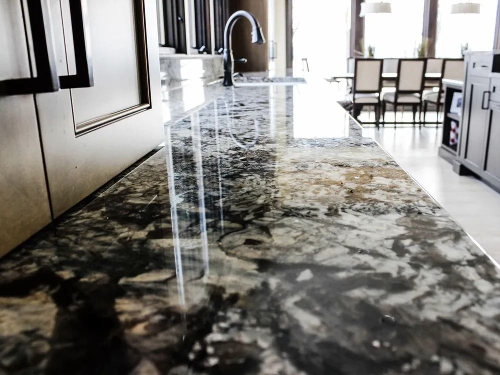 Close-up of a granite countertop with a reflective surface, a faucet, and a view into a dining area.