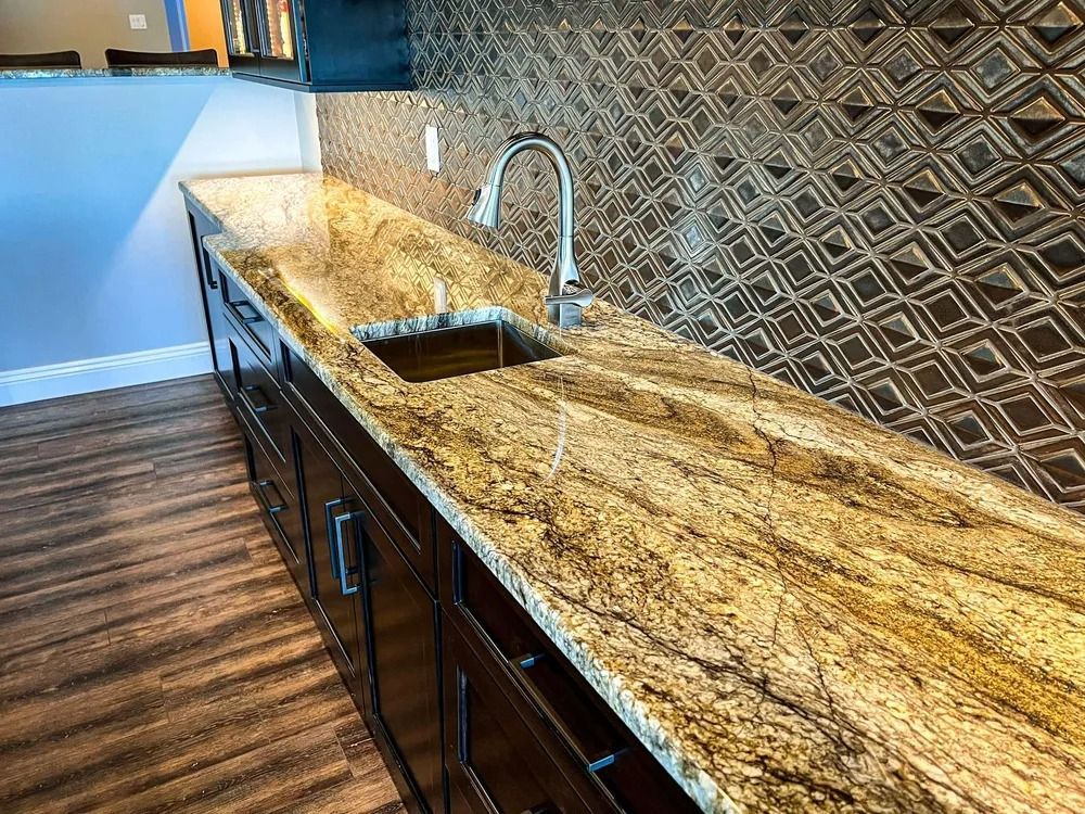 Kitchen countertop with granite surface, sink, faucet, dark cabinets, decorative backsplash, wood flooring.