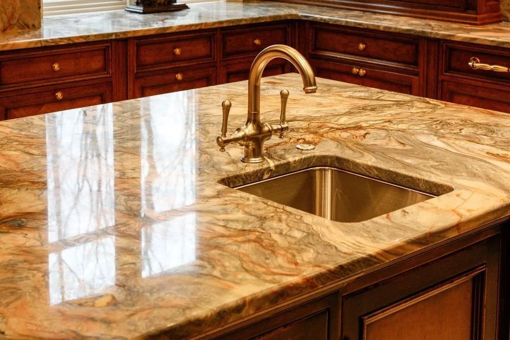Stainless steel sink set in a granite countertop with a bronze faucet, surrounded by dark wooden cabinets.