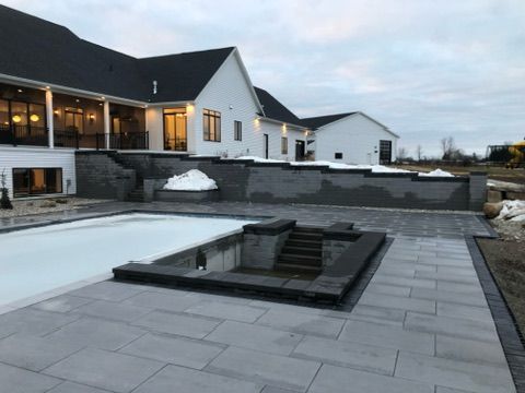 A modern white house with a black roof overlooks a grey stone patio, a covered pool, and a sunken seating area.