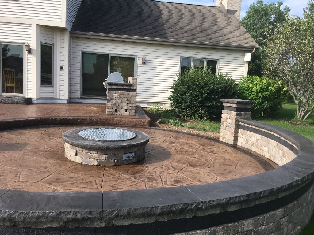 A backyard patio featuring a circular stone fire pit and a curved retaining wall with dark stone accents.