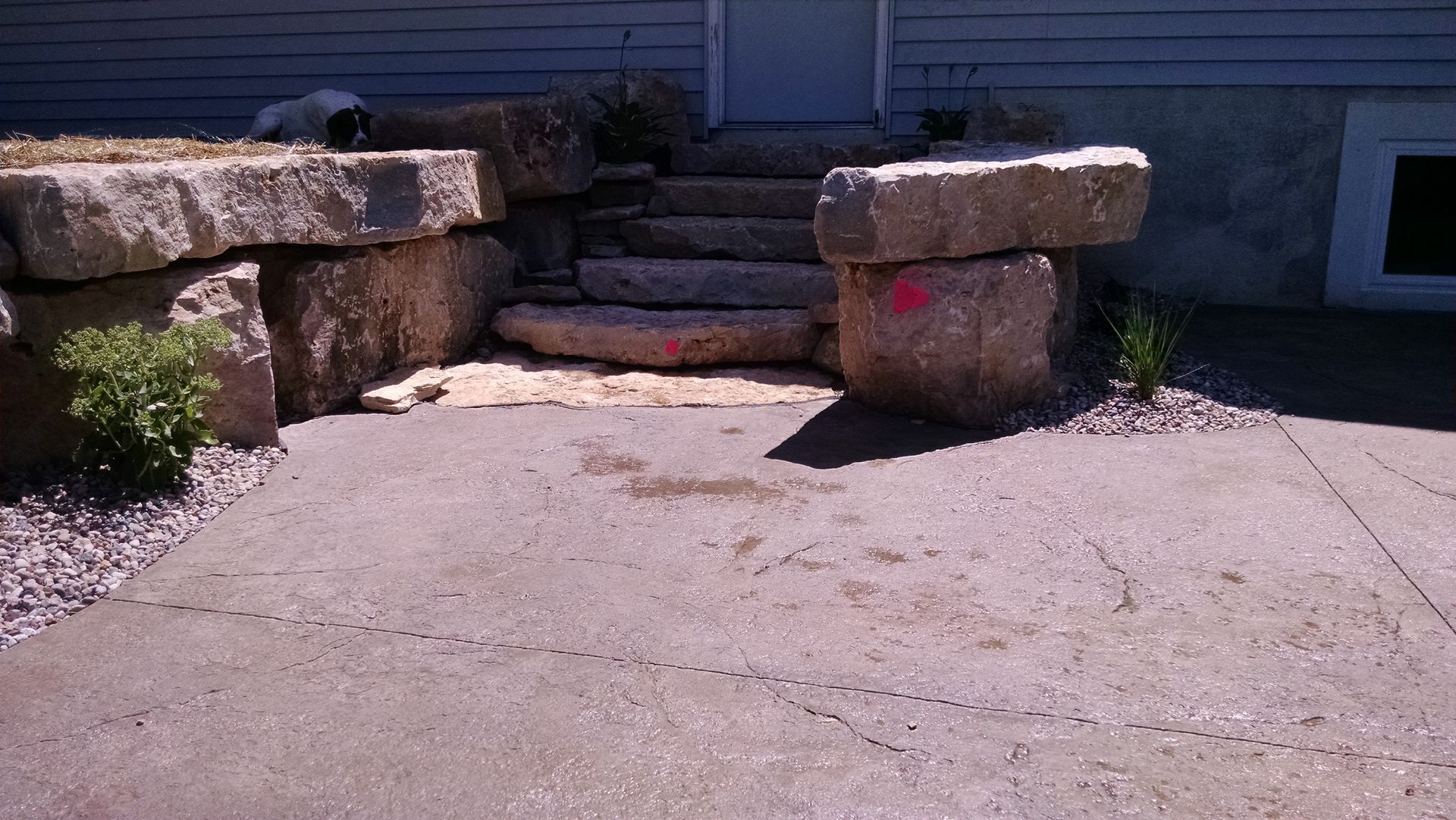 Stone steps leading to a house entrance, flanked by large natural stone retaining walls and a concrete patio.
