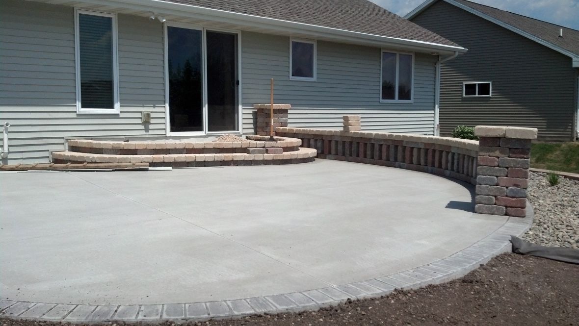 A newly paved circular concrete patio with brick-edged stairs and a low stone retaining wall against a house exterior.