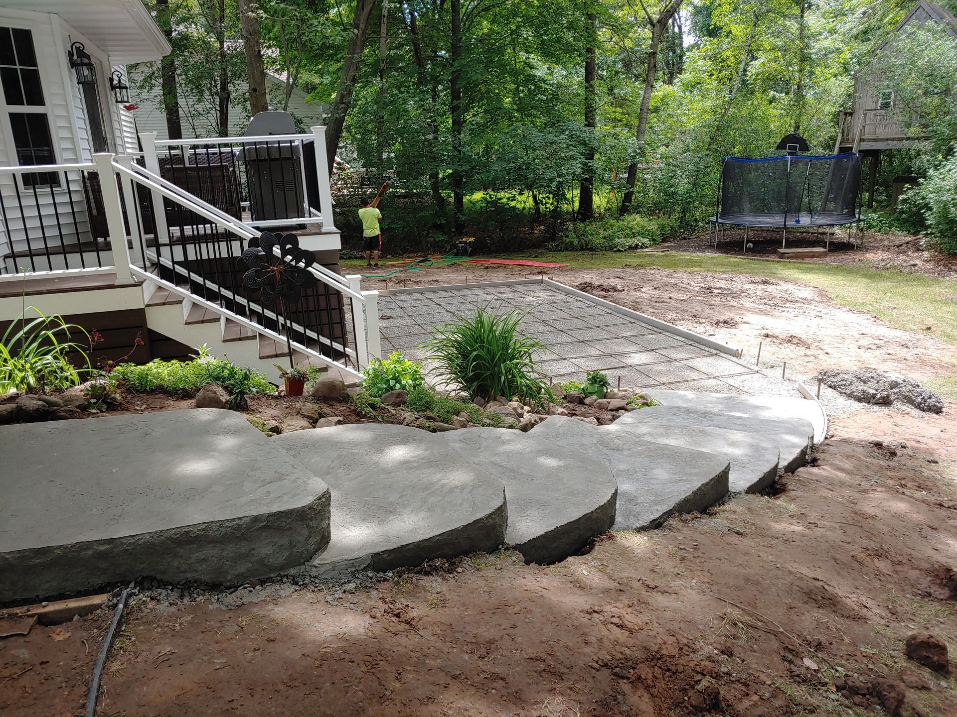 A set of concrete stairs leading from a house deck down to a partially paved backyard area surrounded by trees.