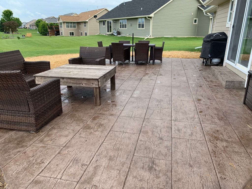 A patio with a brown stamped-concrete floor, a wooden coffee table, matching wicker chairs, and a dining set.