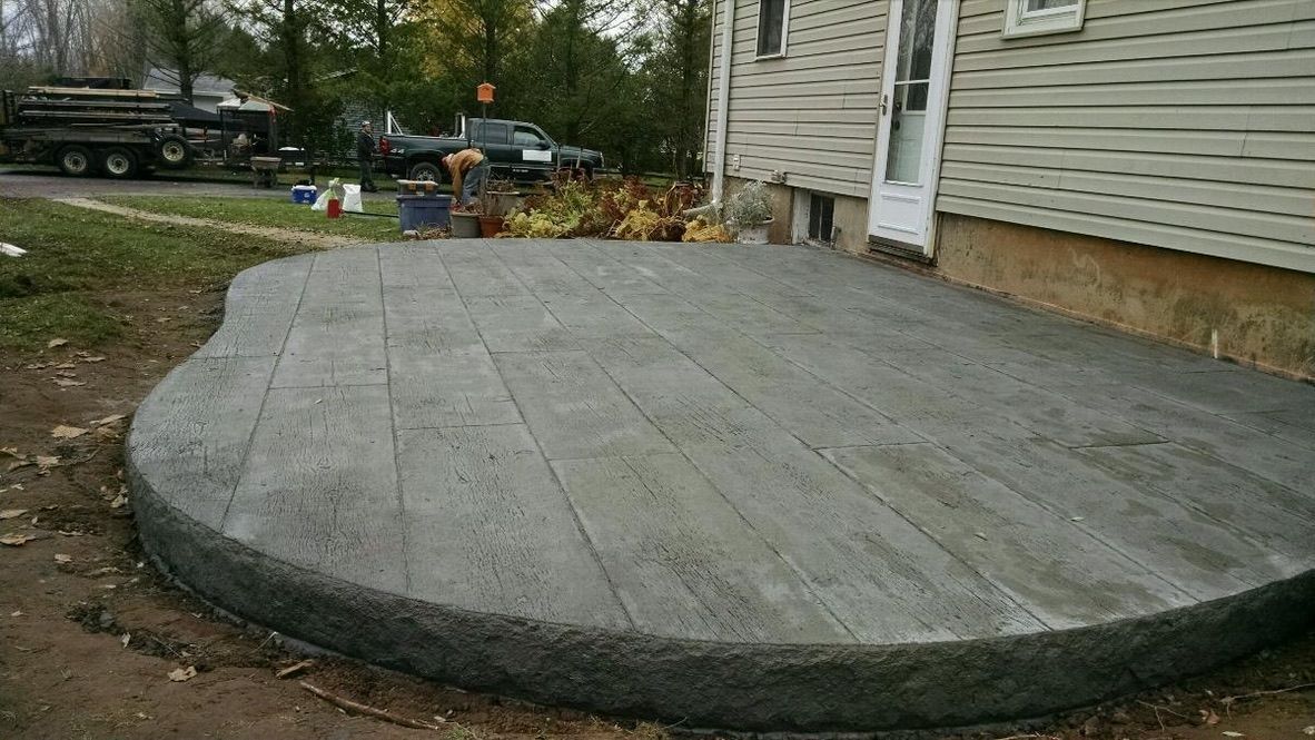 A new concrete patio with a wood-plank stamp texture outside a house with beige siding.