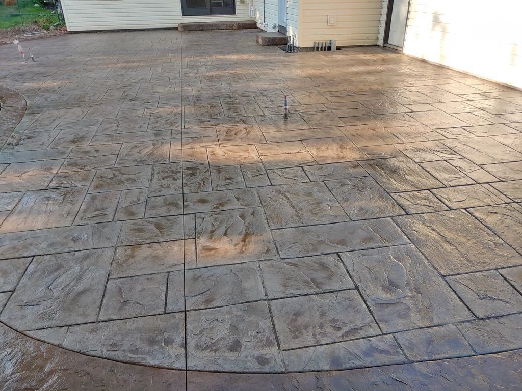A stamped concrete patio featuring a textured, ashlar-patterned design in shades of gray and brown next to a house.