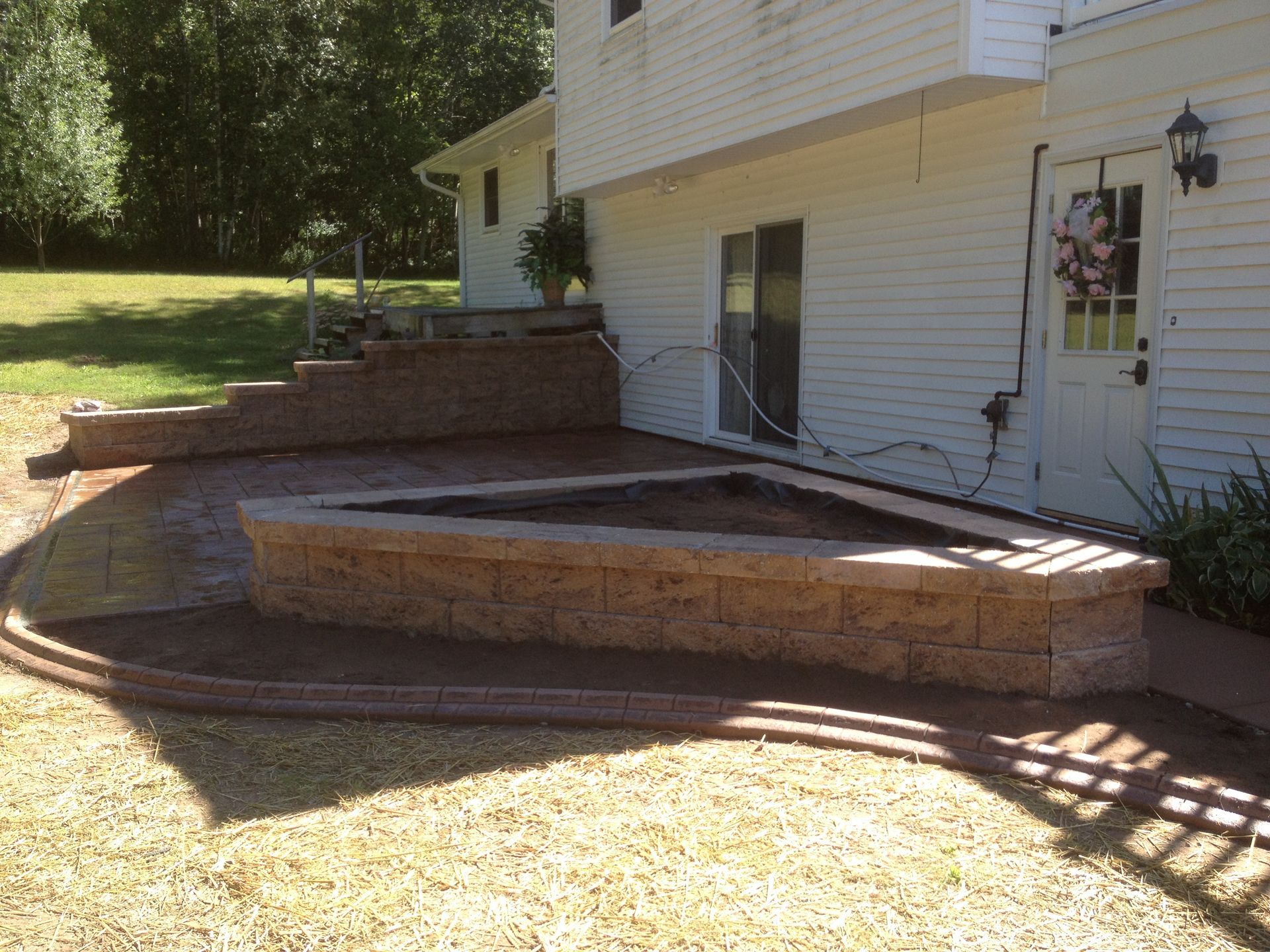 A tan stone retaining wall and patio area next to a white house with sliding glass doors and a back door.