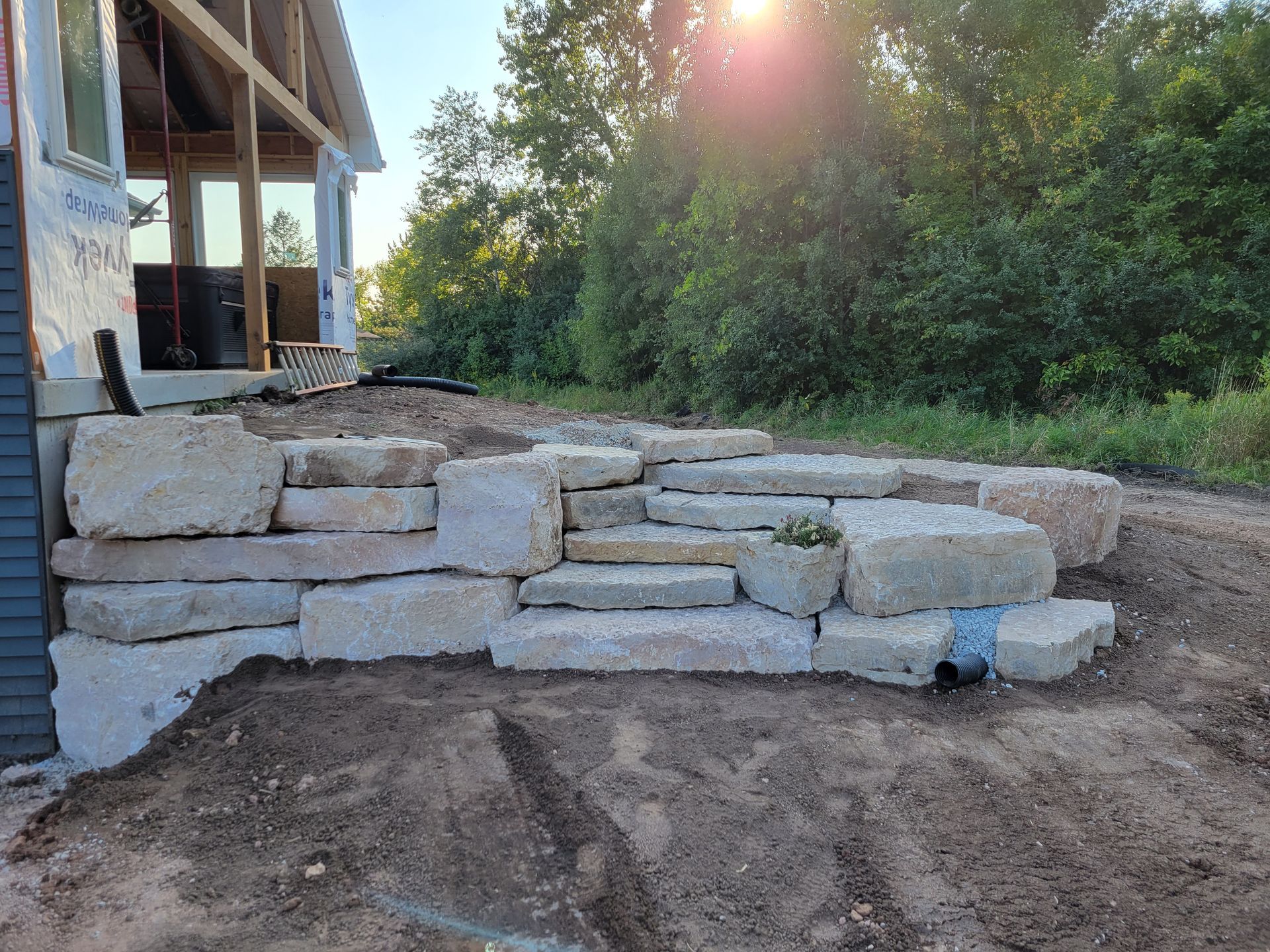 Large, light-colored stone steps and a retaining wall newly built against the side of a house under construction.
