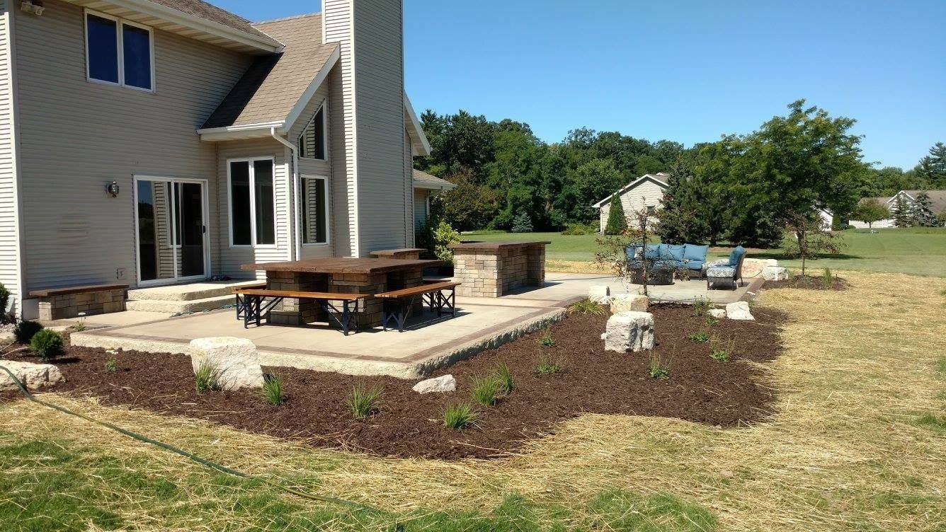 Backyard patio featuring a dining set, stone bar, and landscaped mulch garden area adjacent to a two-story home.