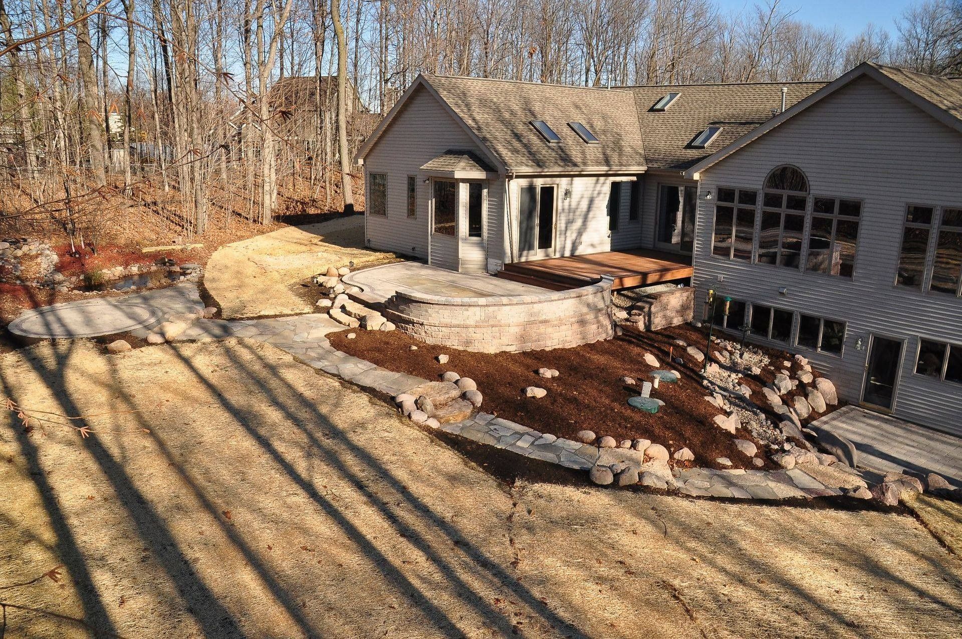 An elevated view of a house exterior featuring a stone patio, a mulched garden bed, and large landscaping rocks.