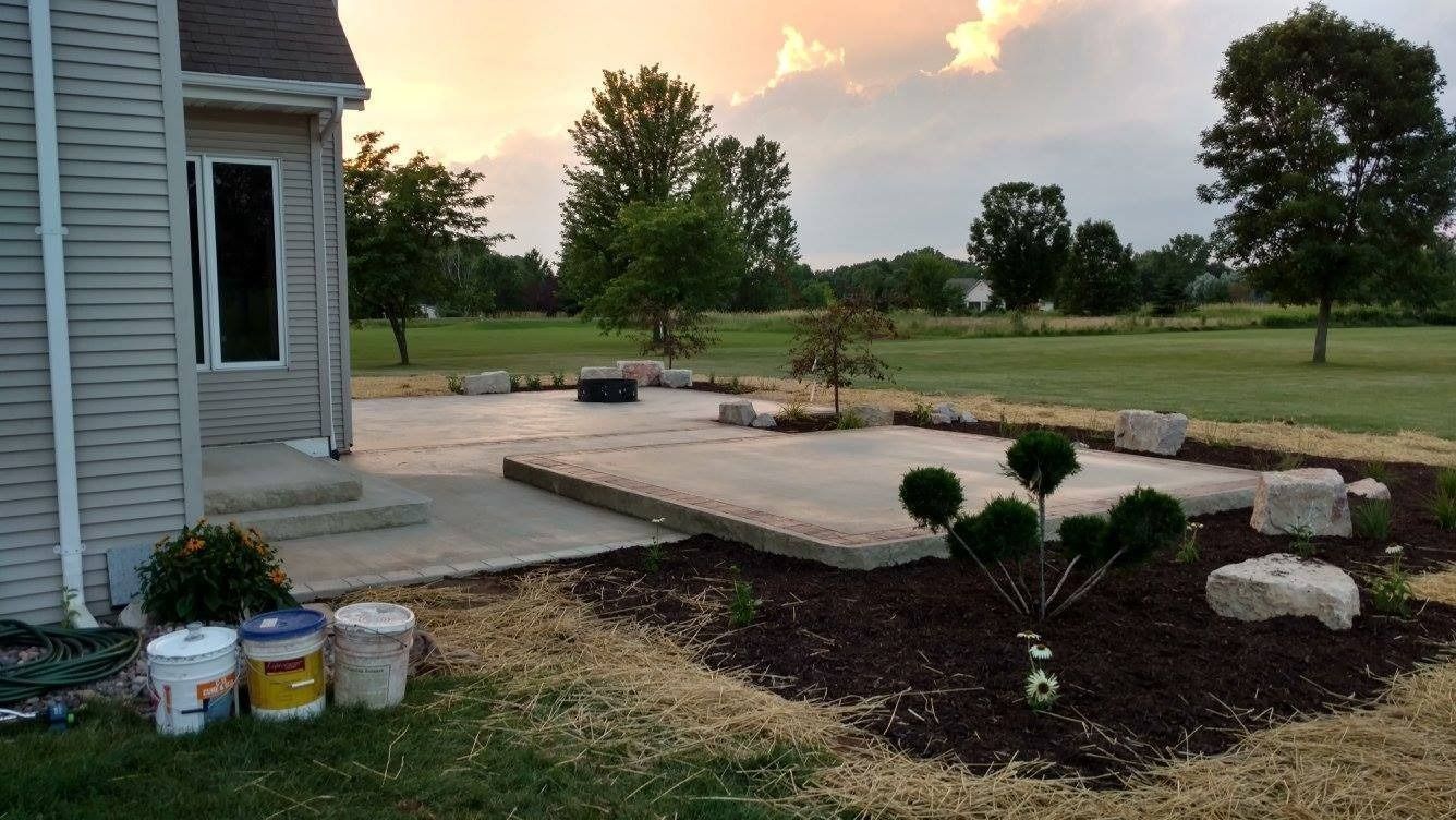 A backyard concrete patio with stone block borders, mulch beds, and a small decorative shrub at sunset.