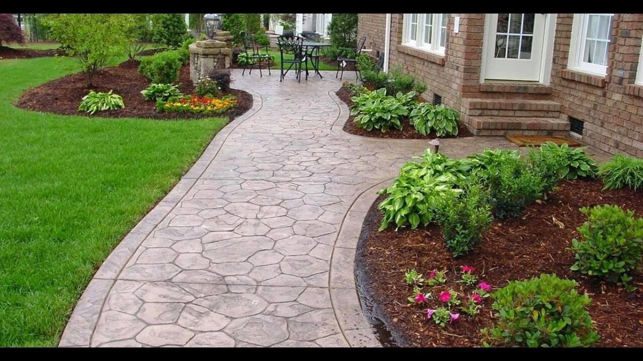 A curved stamped concrete walkway leads to a brick home, surrounded by lush green lawns and mulched garden beds.