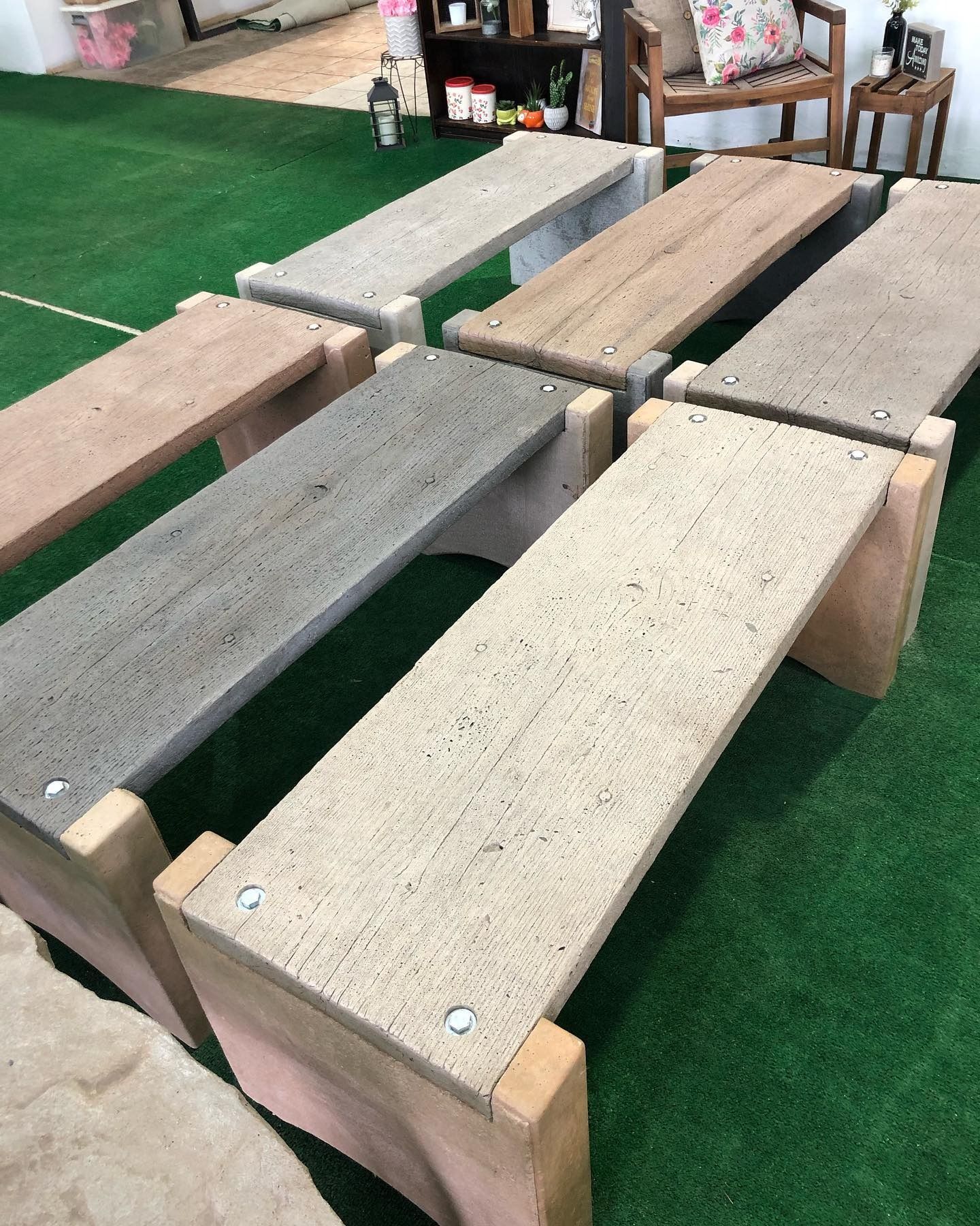Several long, rectangular benches with varied concrete-textured tops and wooden leg supports sit on green artificial turf.