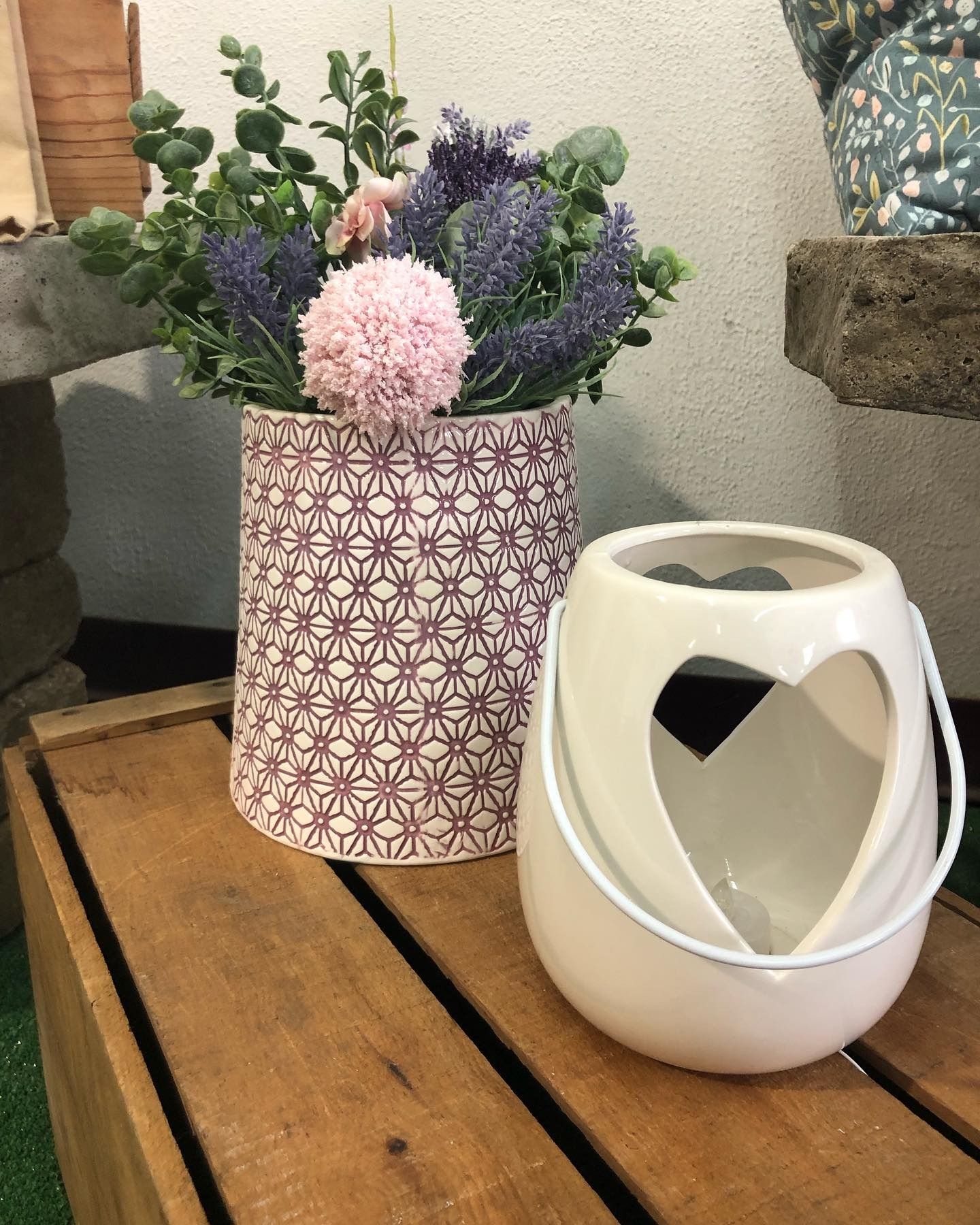 A decorative floral arrangement in a patterned vase sits next to a white ceramic lantern with a heart-shaped cutout.