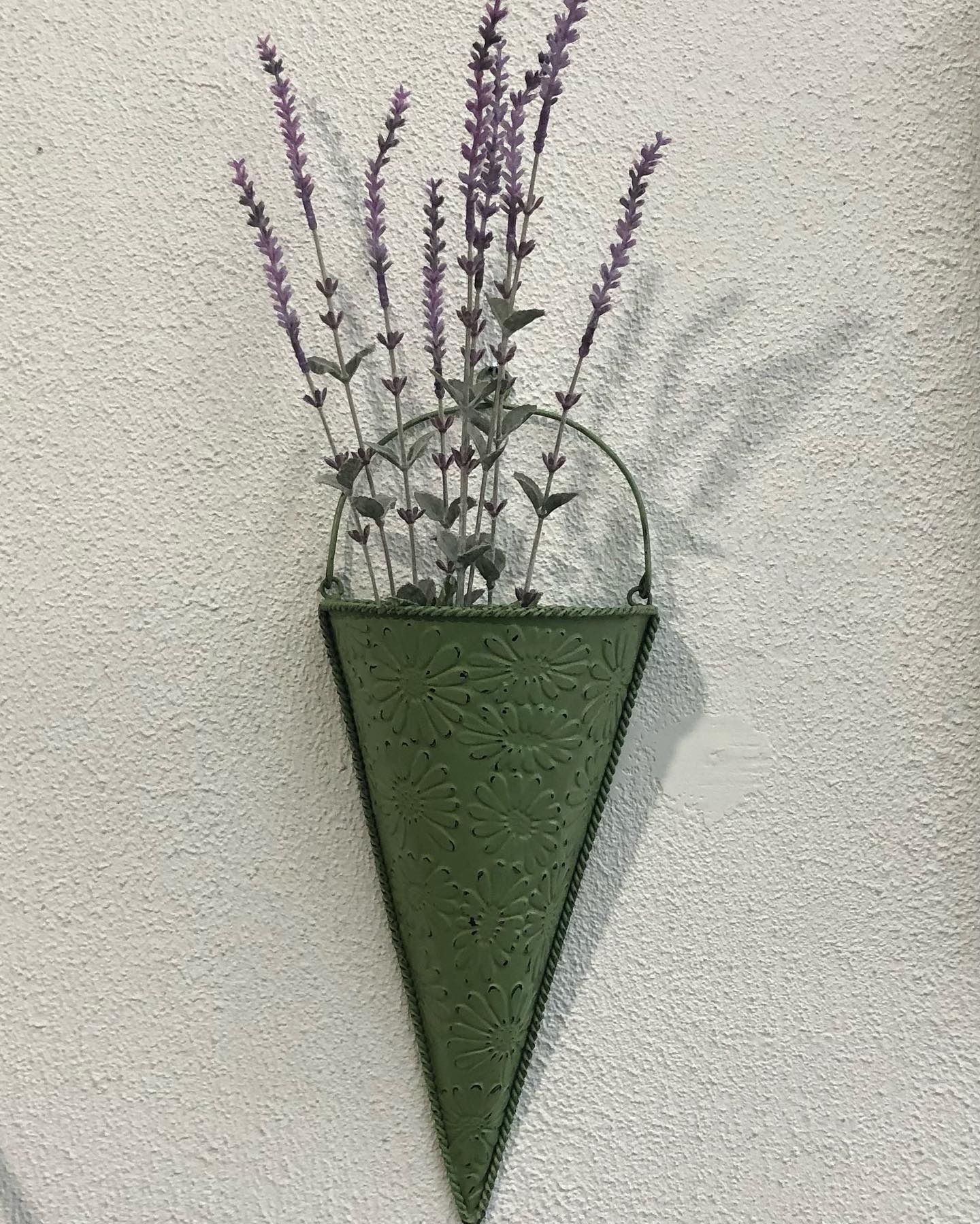 A cone-shaped, olive green metal wall planter with an embossed pattern, holding sprigs of purple lavender.
