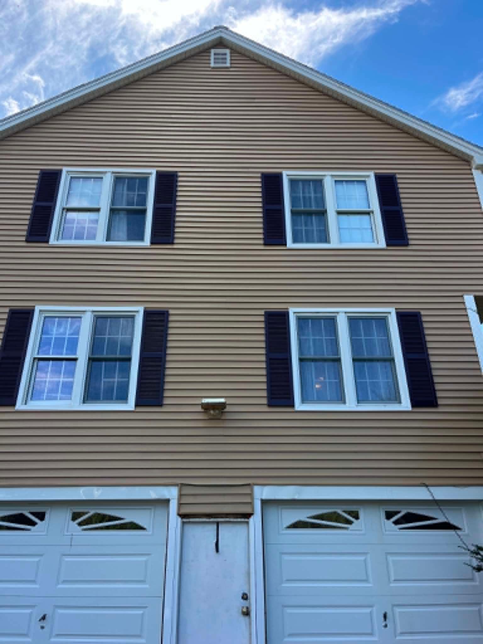 Three-story beige townhouse with black shutters and two white garage doors under a blue sky