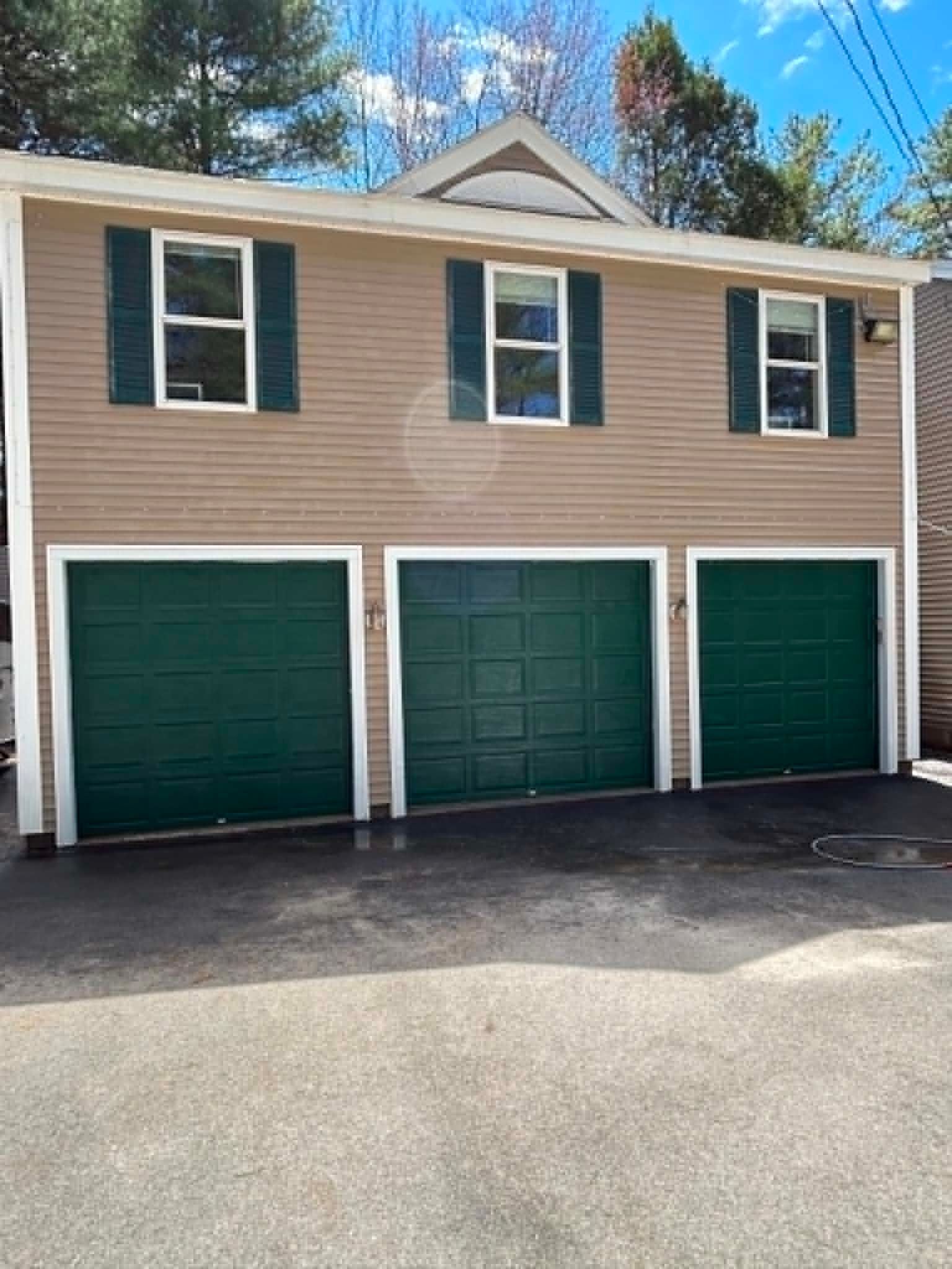 Three green garage doors on a beige two-story garage with white trim under a blue sky