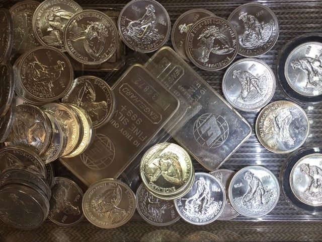 A pile of silver coins and a silver bar