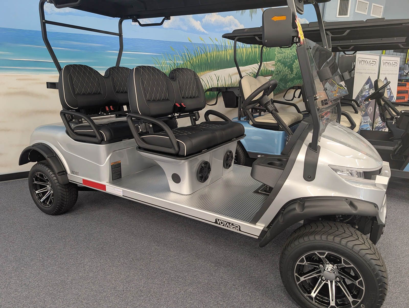 Silver six-seat golf cart with black seats, black wheels, and a black roof