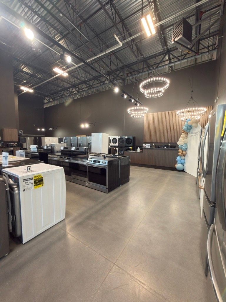 Modern appliance showroom with washers, dryers, and kitchen displays under high industrial ceiling lights