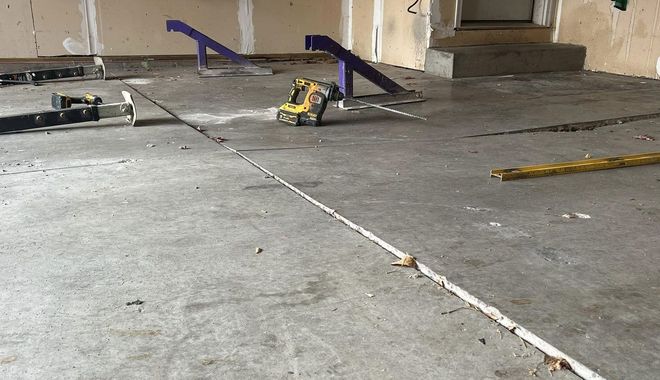 Concrete floor in a partially built room with construction tools and a purple saw horse.
