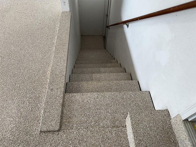 Narrow indoor stairwell with gray carpeted steps, white walls, and a wooden handrail