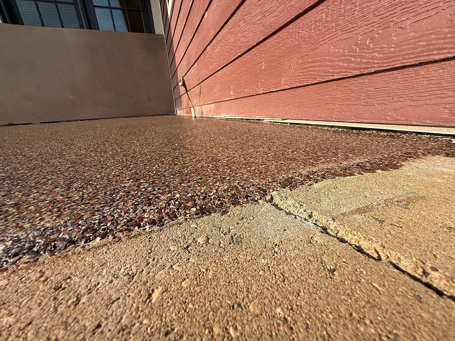 Ground-level view of a gravel walkway beside a red brick wall and tan concrete paving.