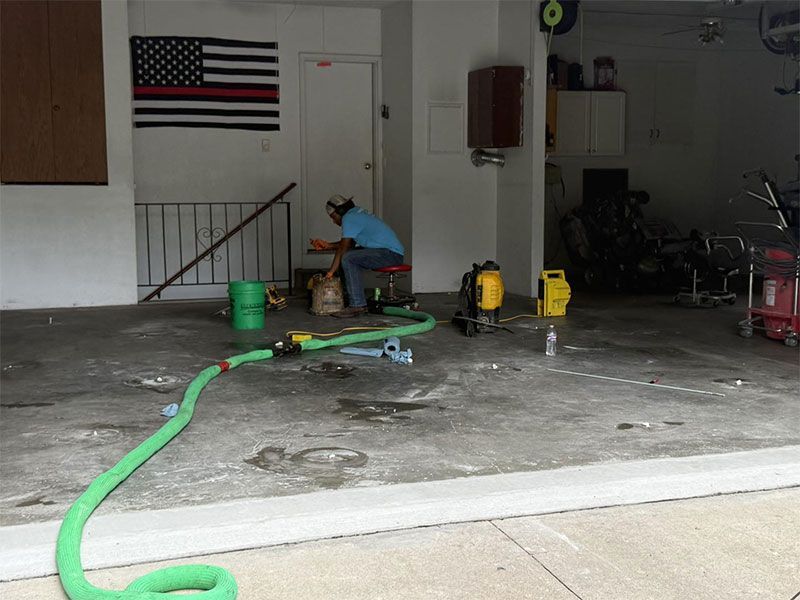 Garage with a green hose on the floor, tools and equipment, and a person working near the back wall