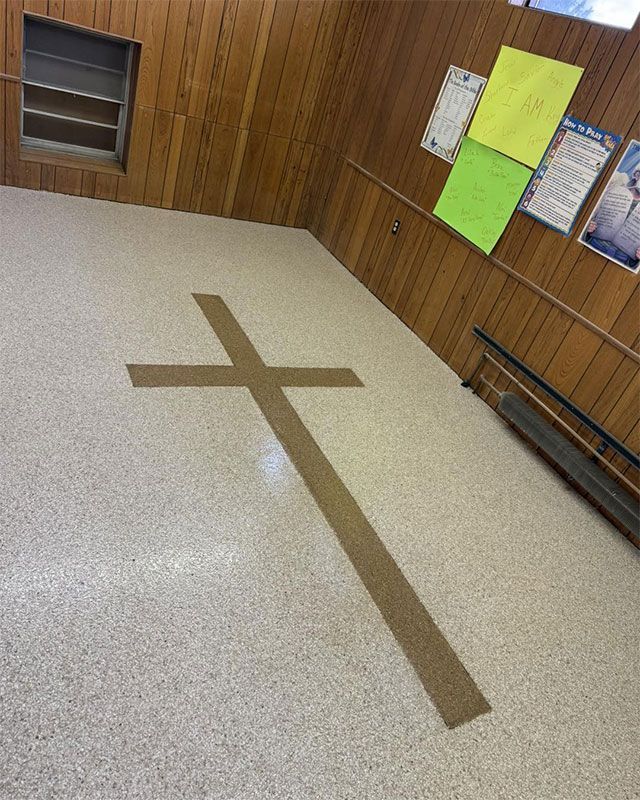 Wood-paneled hallway with a taped brown cross on the floor and bright notices on the wall