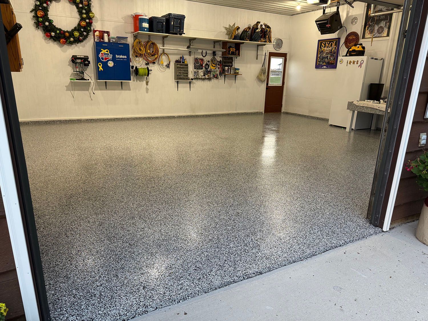 Spacious garage with speckled epoxy floor, wall-mounted tools, and a decorated wreath on the left wall.