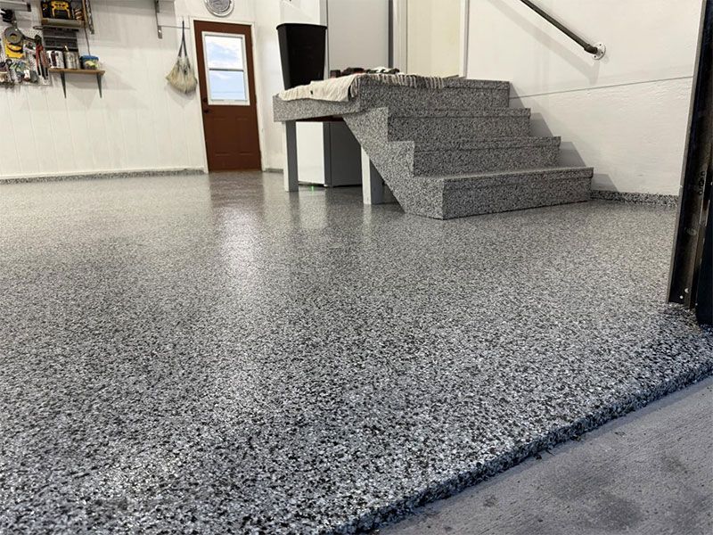 Empty indoor stairwell with gray speckled flooring and a wooden door in the background