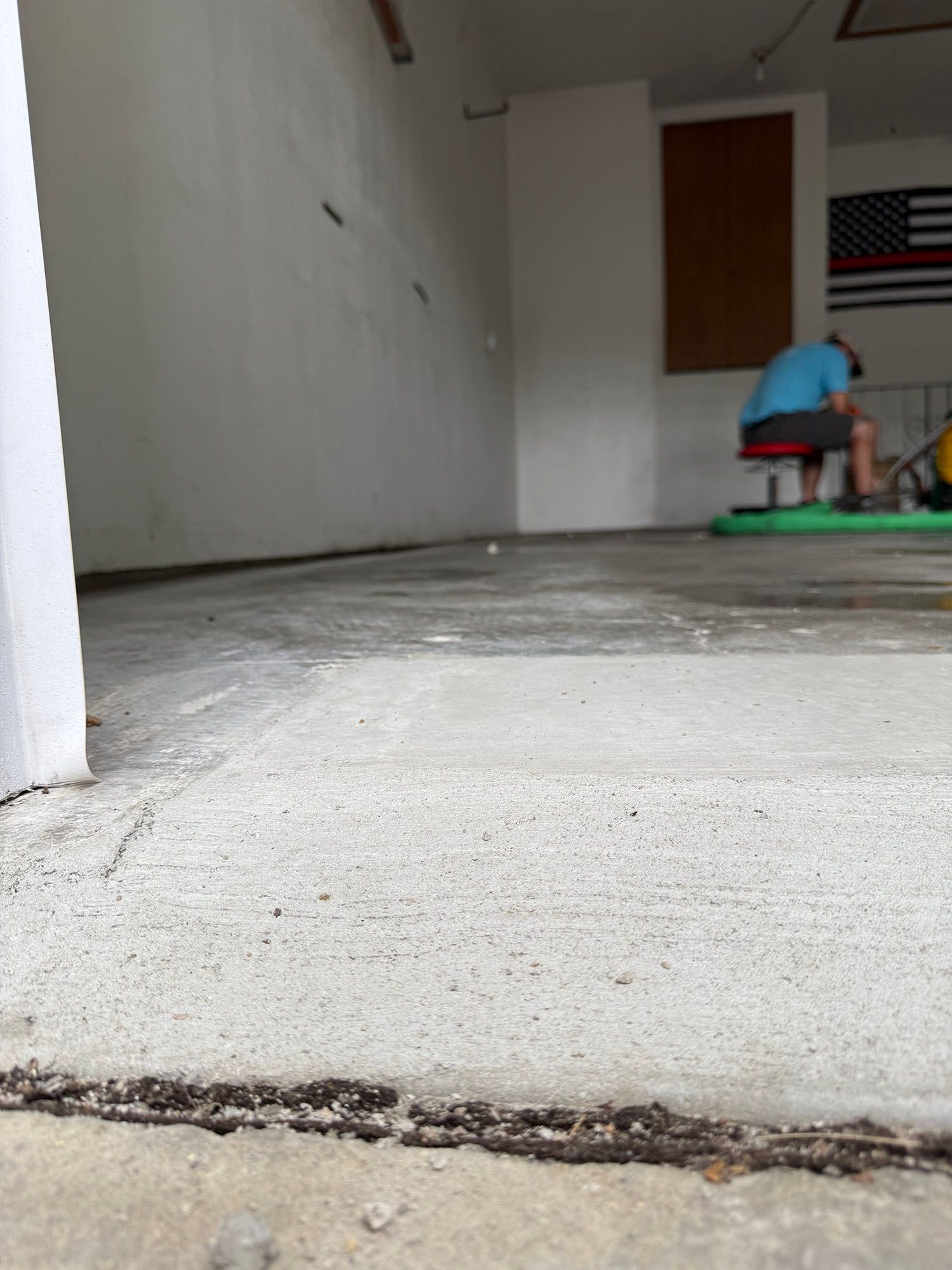 Bare concrete floor in unfinished room, with a person working near the back wall.