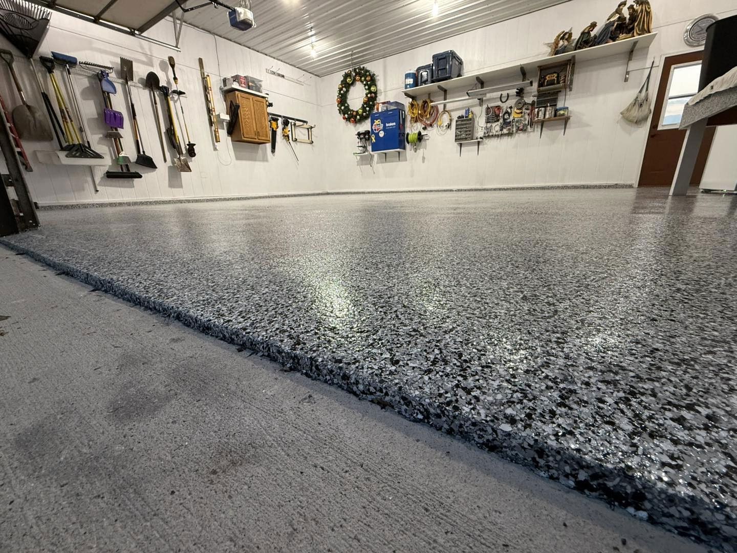 Garage with freshly coated epoxy floor, showing a speckled gray surface and hanging tools on the wall.