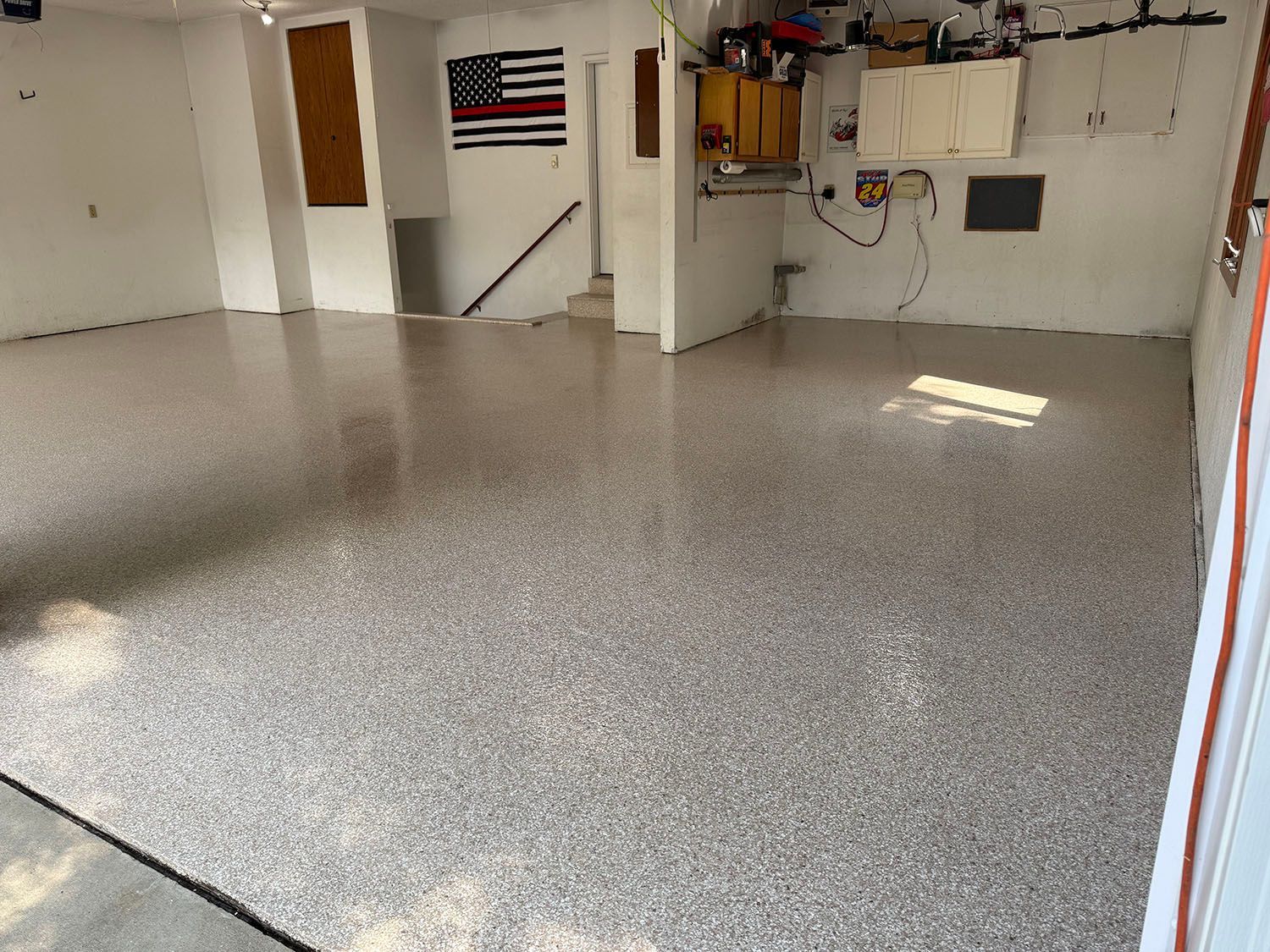 Empty garage with speckled epoxy floor, white walls, and an American flag on the back wall.