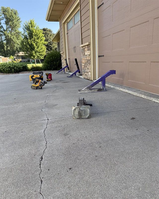 Concrete walkway beside beige building, with a crack, small tools, and purple wheelbarrow handles.