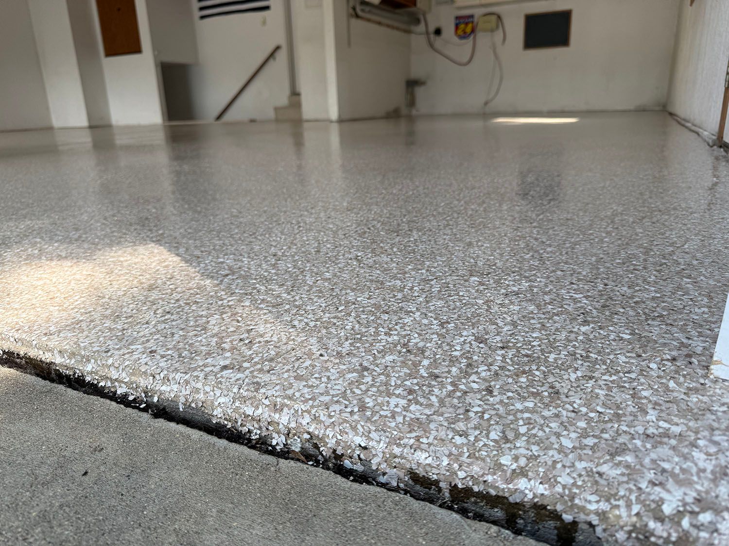 Close-up of speckled epoxy garage floor with a raised crack or seam in the foreground.