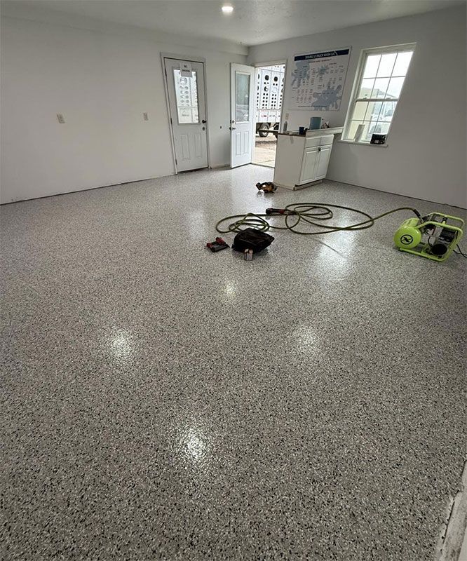 Empty room with speckled epoxy floor and cleaning equipment near the back wall.
