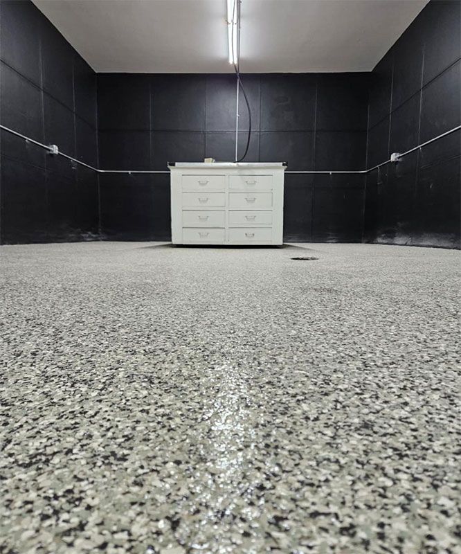 Empty black-walled room with speckled floor and a white dresser under a ceiling light.