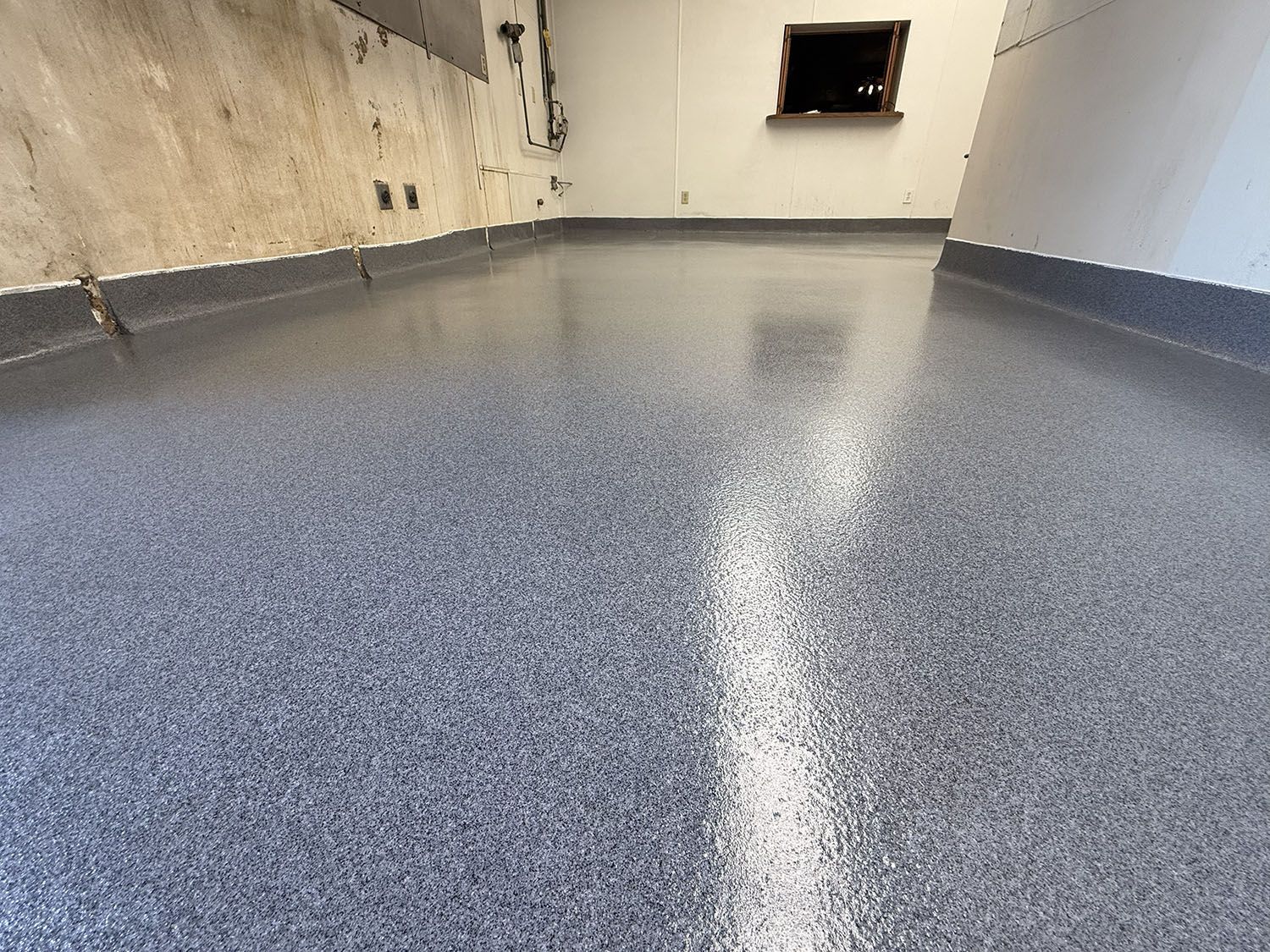 Empty room with glossy gray speckled floor and white walls, seen from a low angle.