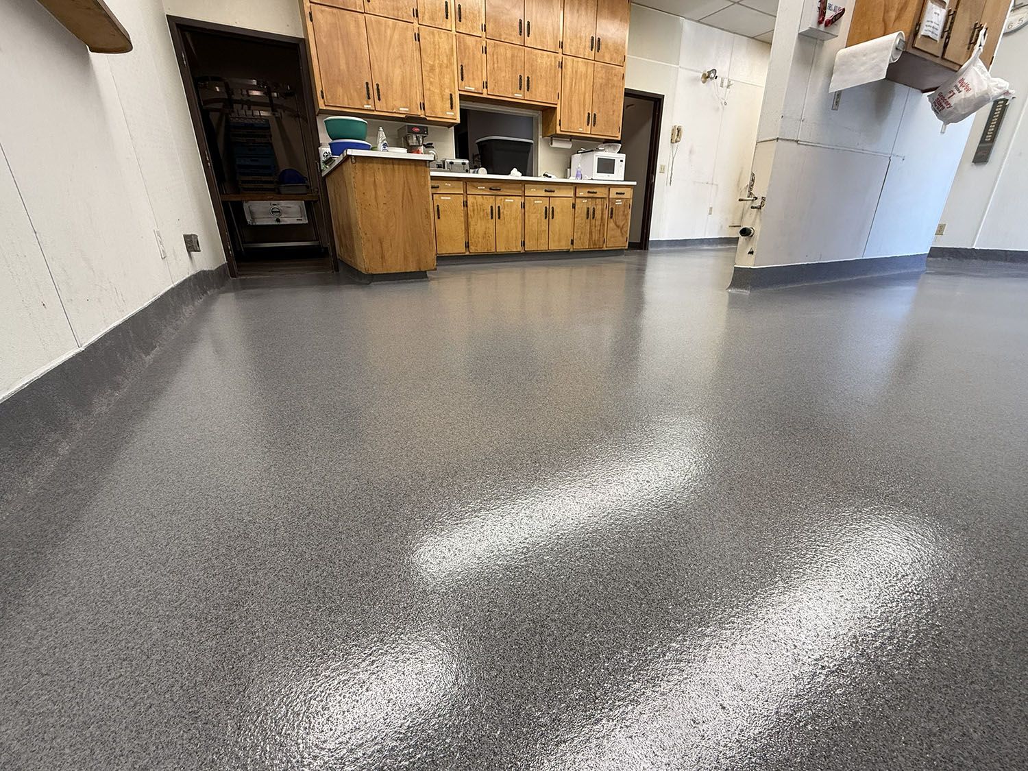 Empty kitchen with speckled gray floor and wooden cabinets along the back wall.