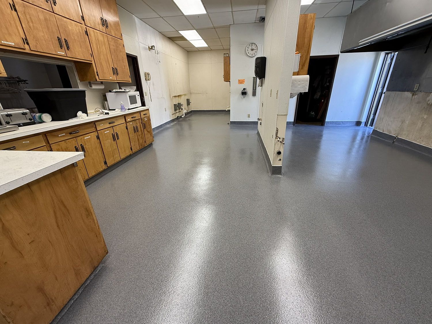 Empty kitchen break room with wood cabinets, gray floor, and white walls.