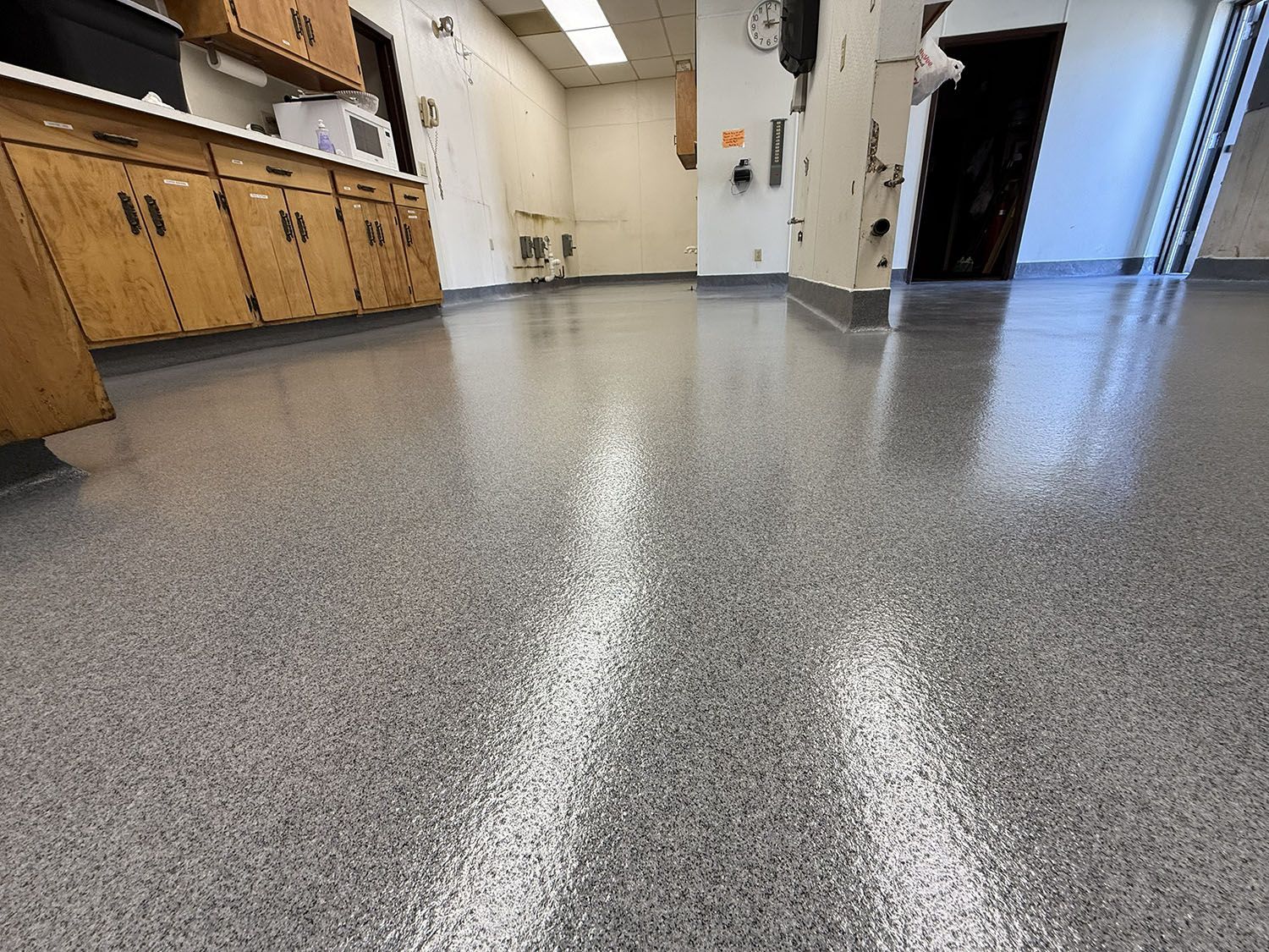 Empty laboratory with speckled gray floor, wooden cabinets, and bright hallway beyond.