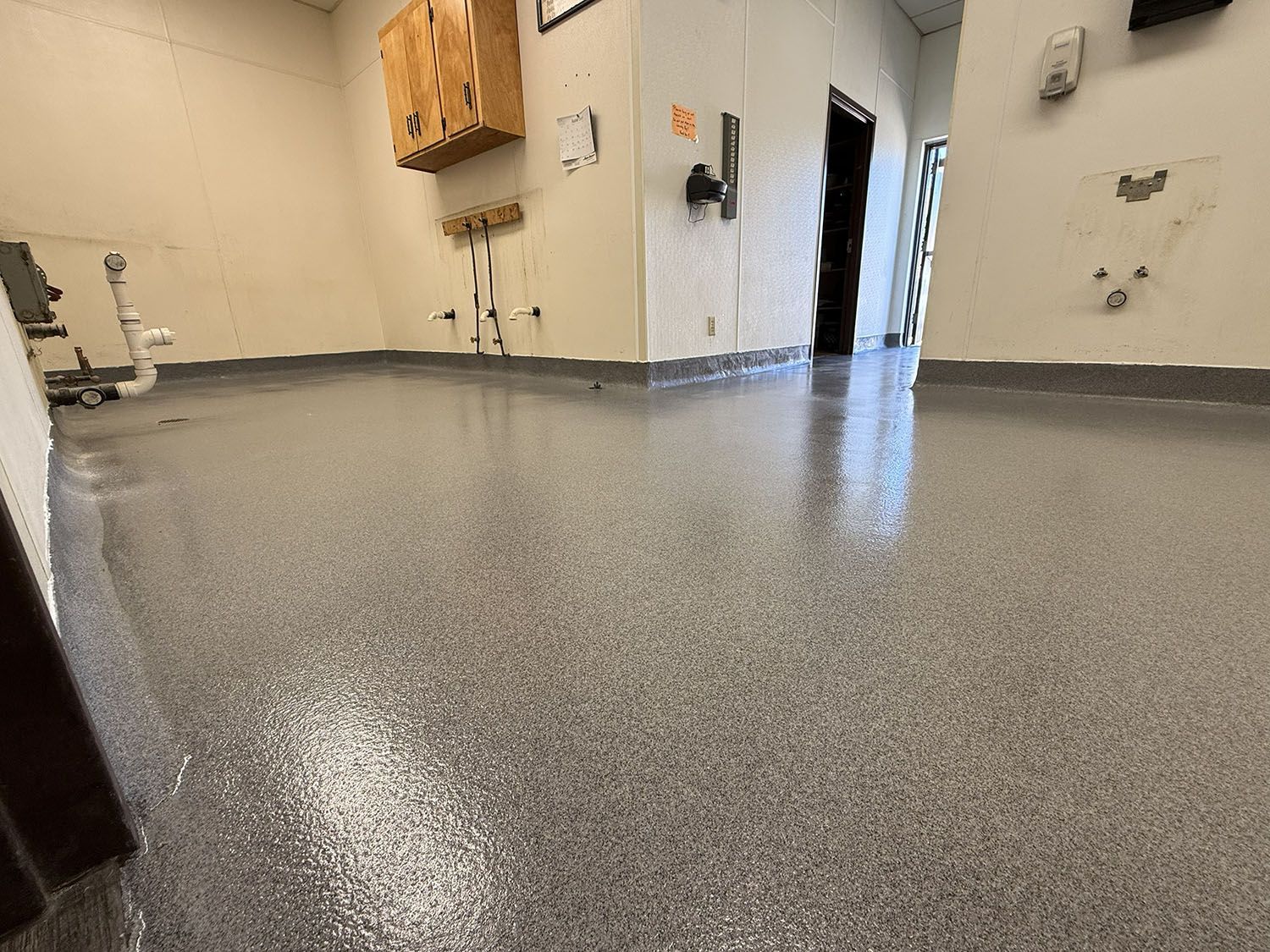 Empty garage floor with gray epoxy coating and open doorway in the background.