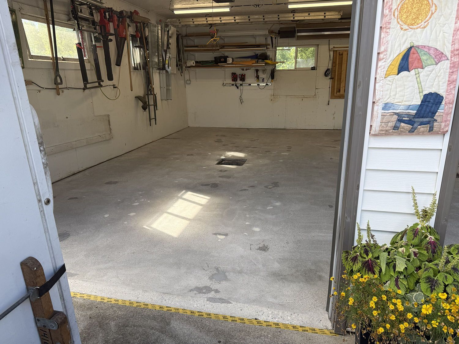 Open garage with concrete floor, hanging tools, and a painted mural on the right wall.