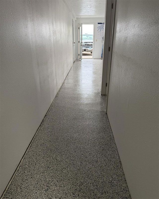Narrow white hallway with speckled gray floor leading to a bright doorway and ocean view.