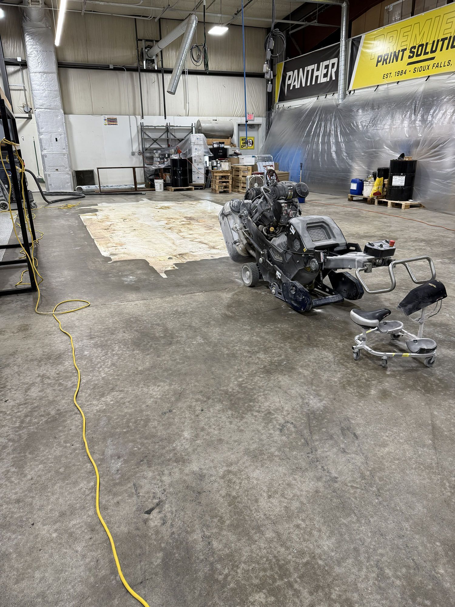 Workshop floor with scattered metal parts, a tarp-covered area, and yellow extension cords near a wall.