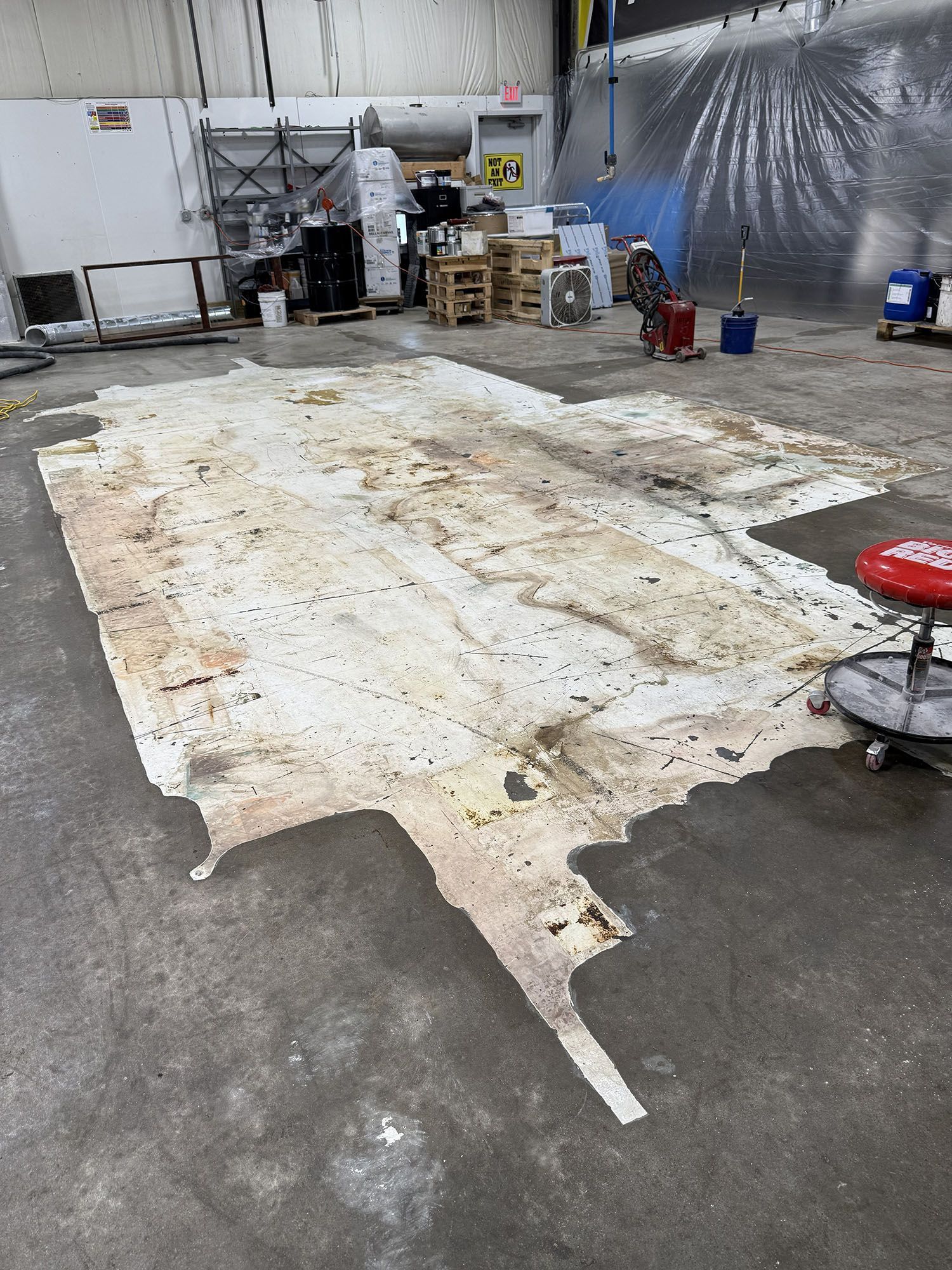 Large white floor covering on a concrete workshop floor with equipment and storage in the background.