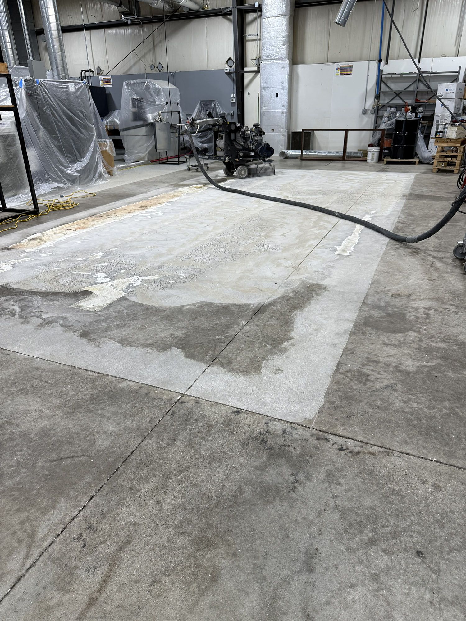Industrial workshop with a concrete floor, machinery, and hanging ducts in the background.