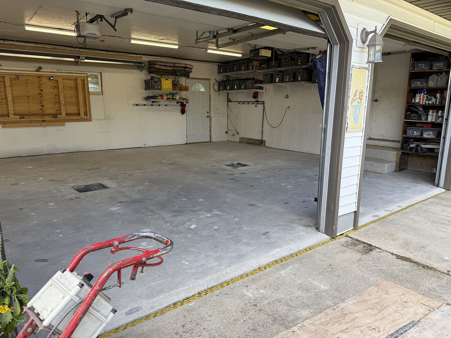 Open garage with empty concrete floor, white walls, shelves, and a red hand truck in the foreground.